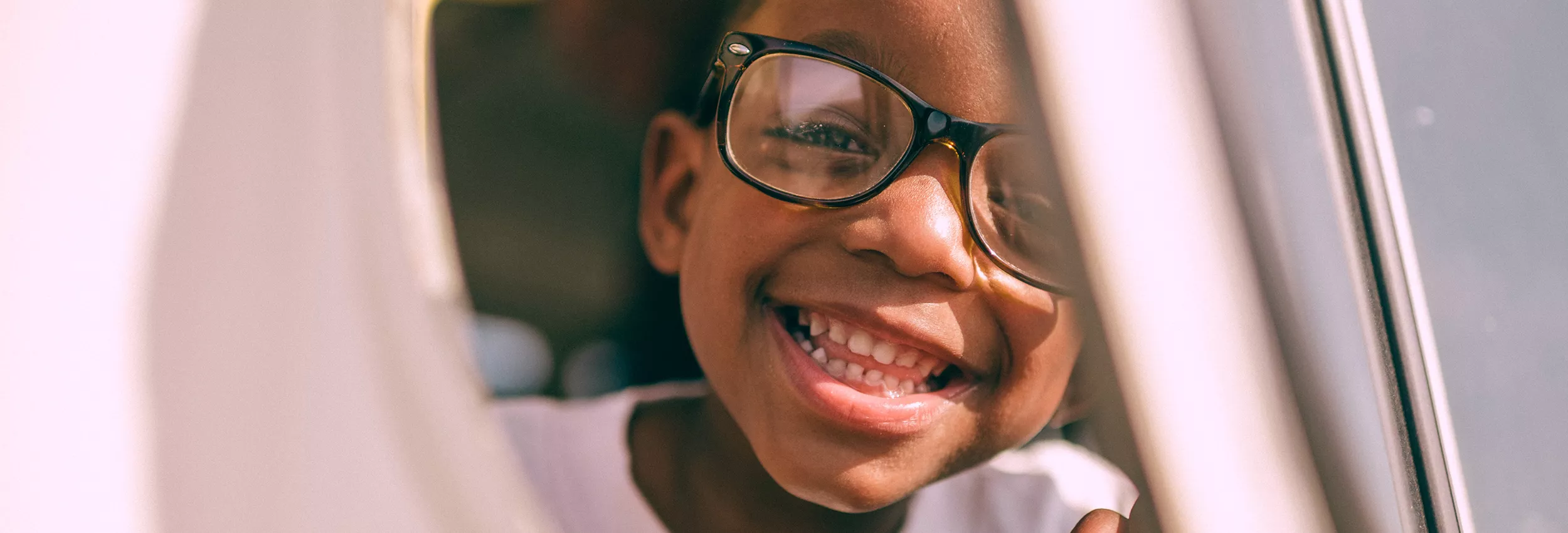 A close-up view of an airplane window with soft, warm lighting. The interior of the aircraft is visible, showcasing a serene travel setting. The image captures a sense of calm and introspection during a flight. The window frame and partial seat detail add context to the travel environment.